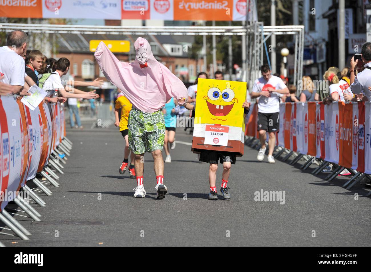 Adult man and boy run dressed as Patrick Star and Sponge Bob square pants for Sports relief cheered on by the crowds in Southampton on the  25th March 2012. Stock Photo