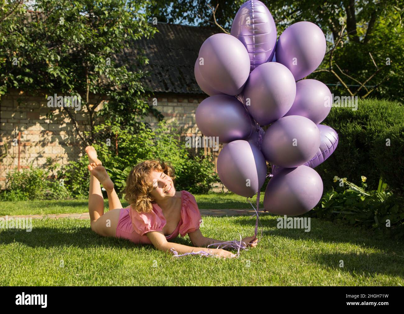 happy beautiful tender girl 17-18 years old with bunch of purple helium balloons lies on green lawn. Birthday girl. Happy day. concept of joy, positiv Stock Photo