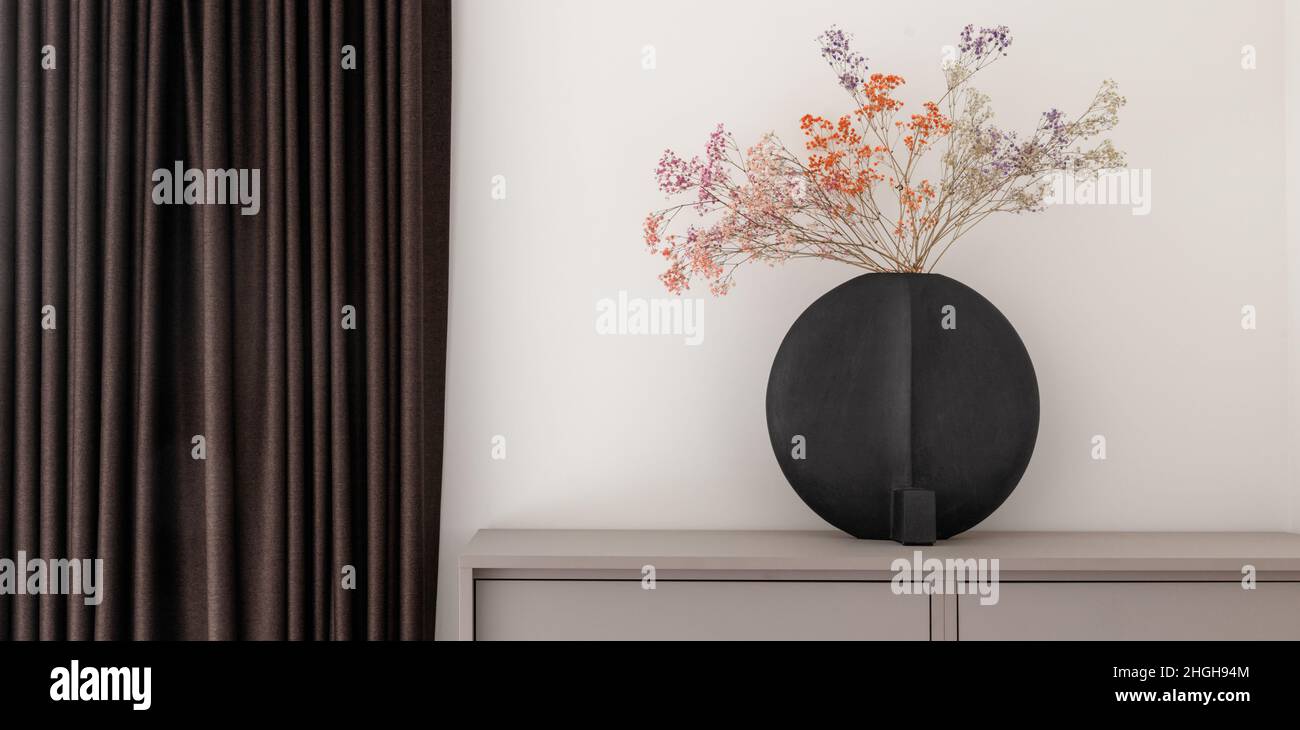 Dried colourful spring flowers in black hand glazed ceramic vase in nordic style against white wall. Minimal interior decoration concept Stock Photo