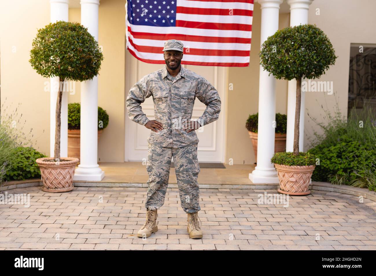 Portrait of smiling african american army man standing with hand on hip against flag on house Stock Photo