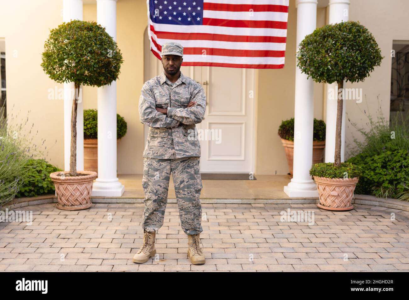 Portrait of confident african american army man in uniform with arms crossed against flag on house Stock Photo