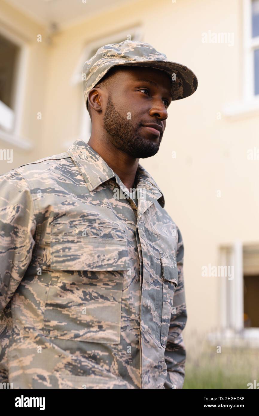 African american army man wearing camouflage uniform and cap looking away against house Stock Photo
