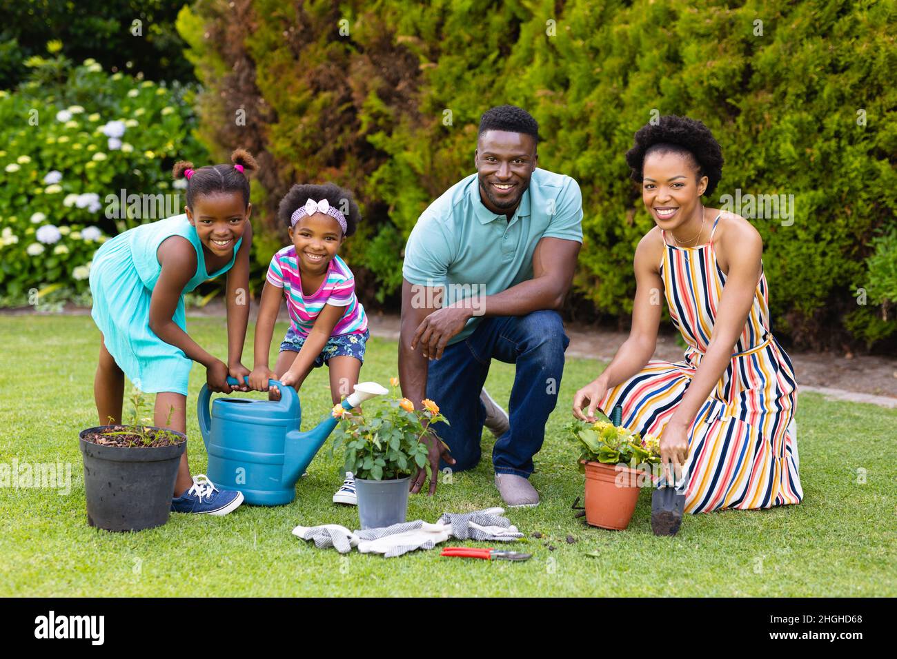 Portrait of happy african american family watering plants together in ...