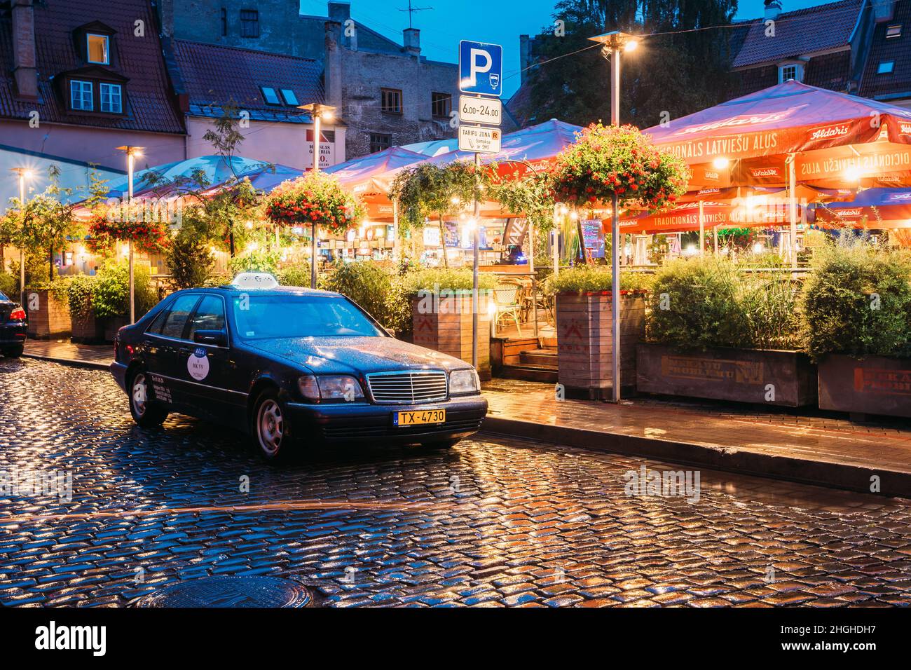 Riga, Latvia. Taxi Car Mercedes-Benz W140 Wait Clients Near Open Air Leisure Venue Recreation Center Egle In Evening Or Night Illumination In Old Town Stock Photo