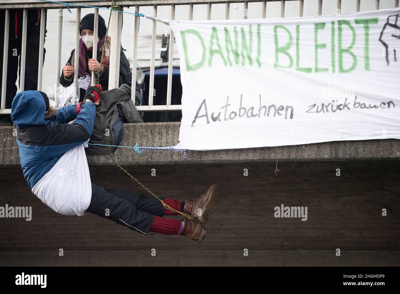 Frankfurt, Germany. Jan 21 2022: An activist hangs on a bridge over the A648 during a demonstration next to a banner reading 'Danni bleibt' and 'Zurück bauen Autobahnen'. The action is taking place as part of a nationwide campaign for a traffic turnaround. In addition, a trial will begin on February 1 in Frankfurt for an abseiling action in the course of the protest against the construction of the A49 and the eviction of the hut village in the Dannenröder Forest. The A648 was completely closed in both directions especially for the action. Photo: Sebastian Gollnow/dpa Credit: dpa picture allian Stock Photo