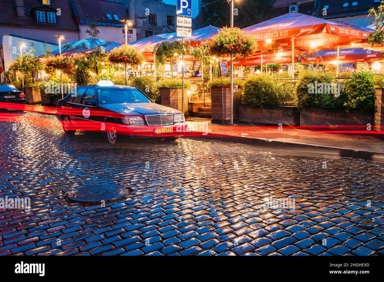 Riga, Latvia. Taxi Car Mercedes-Benz W140 Wait Clients Near Open Air Leisure Venue Recreation Center Egle In Evening Or Night Illumination In Old Town Stock Photo