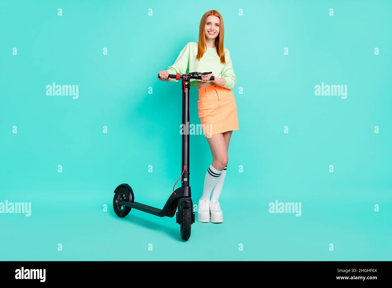 Full size photo of lovely millennial lady stand scooter wear sport clothes isolated on vivid teal color background Stock Photo