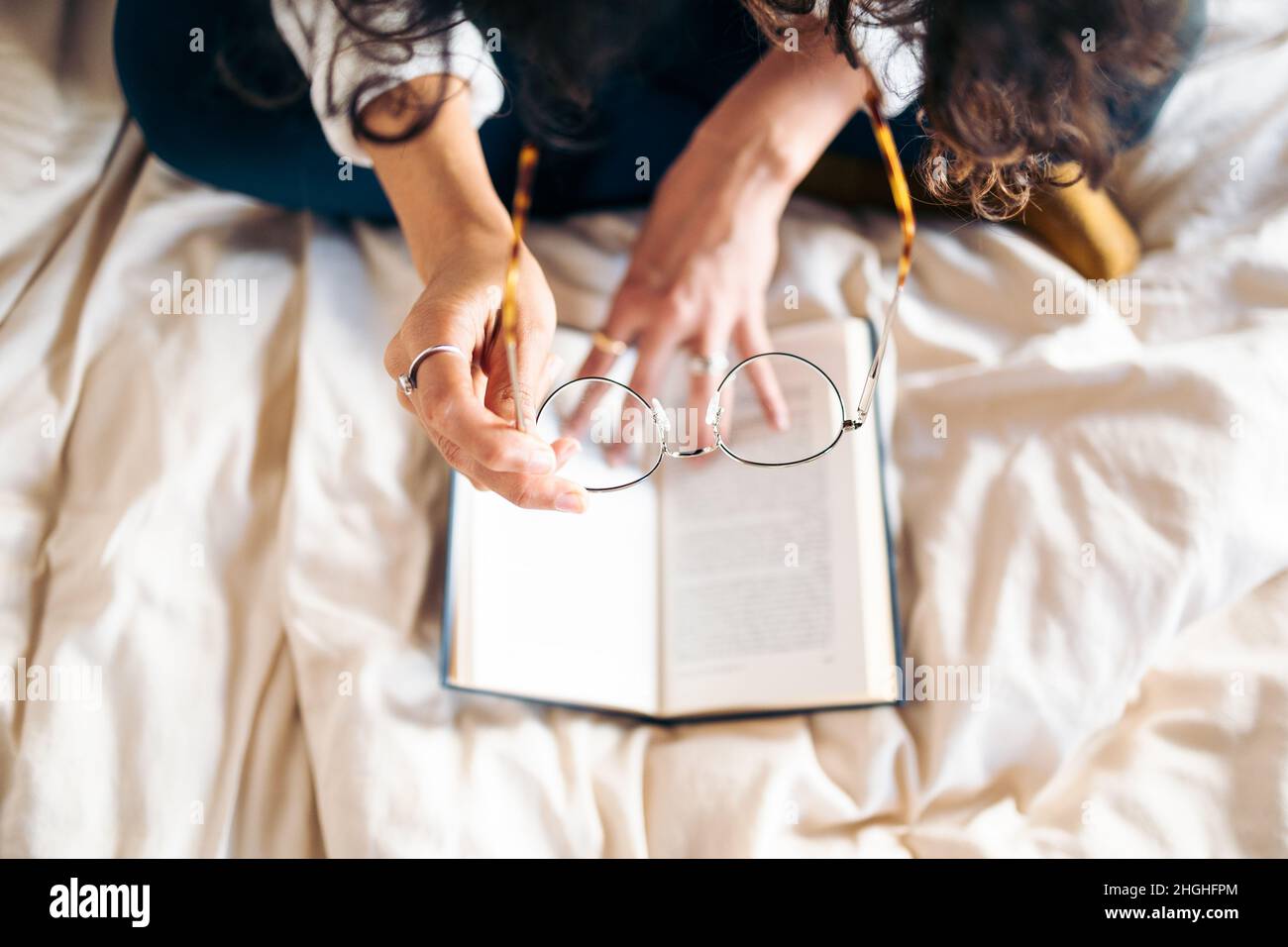 Unrecognizable young woman putting on her glasses to read a book in bed