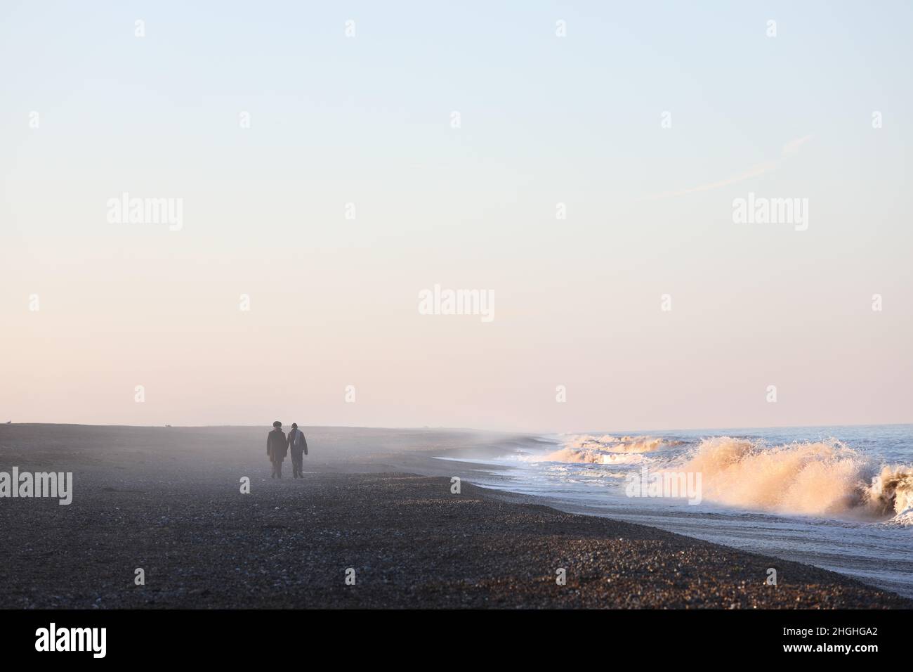 Two people walking hand in hand on a deserted beach surrounded by sea mist in Norfolk, England, UK Stock Photo