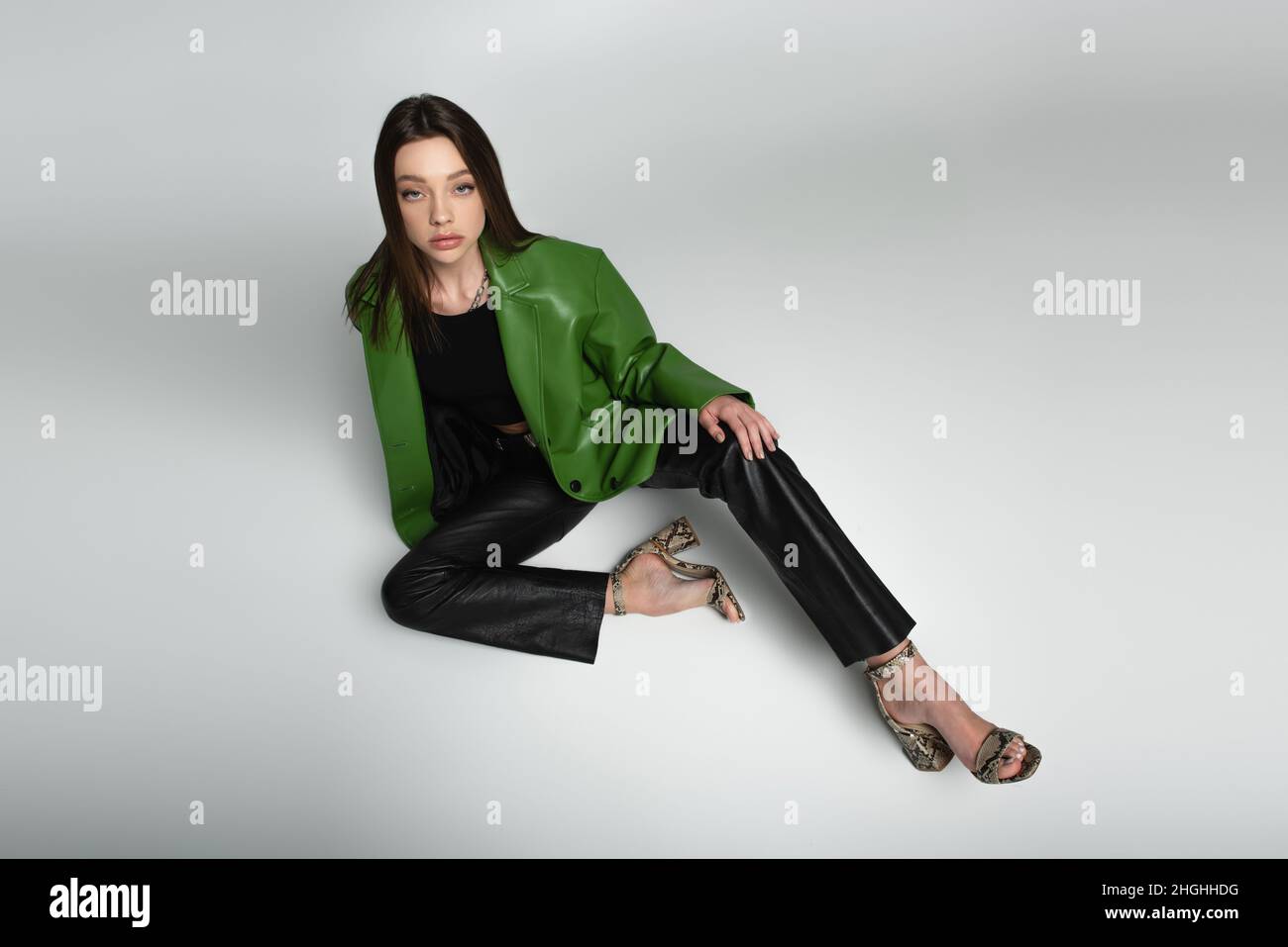 high angle view of woman in black trousers, green jacket and sandals sitting on grey Stock Photo