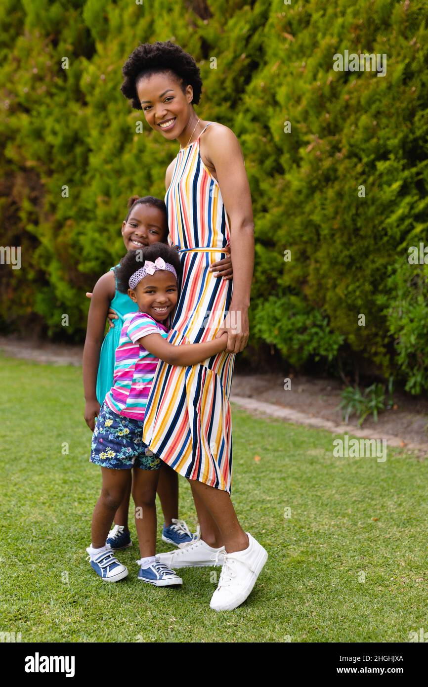 Full length portrait of smiling african american woman embracing daughters at garden Stock Photo