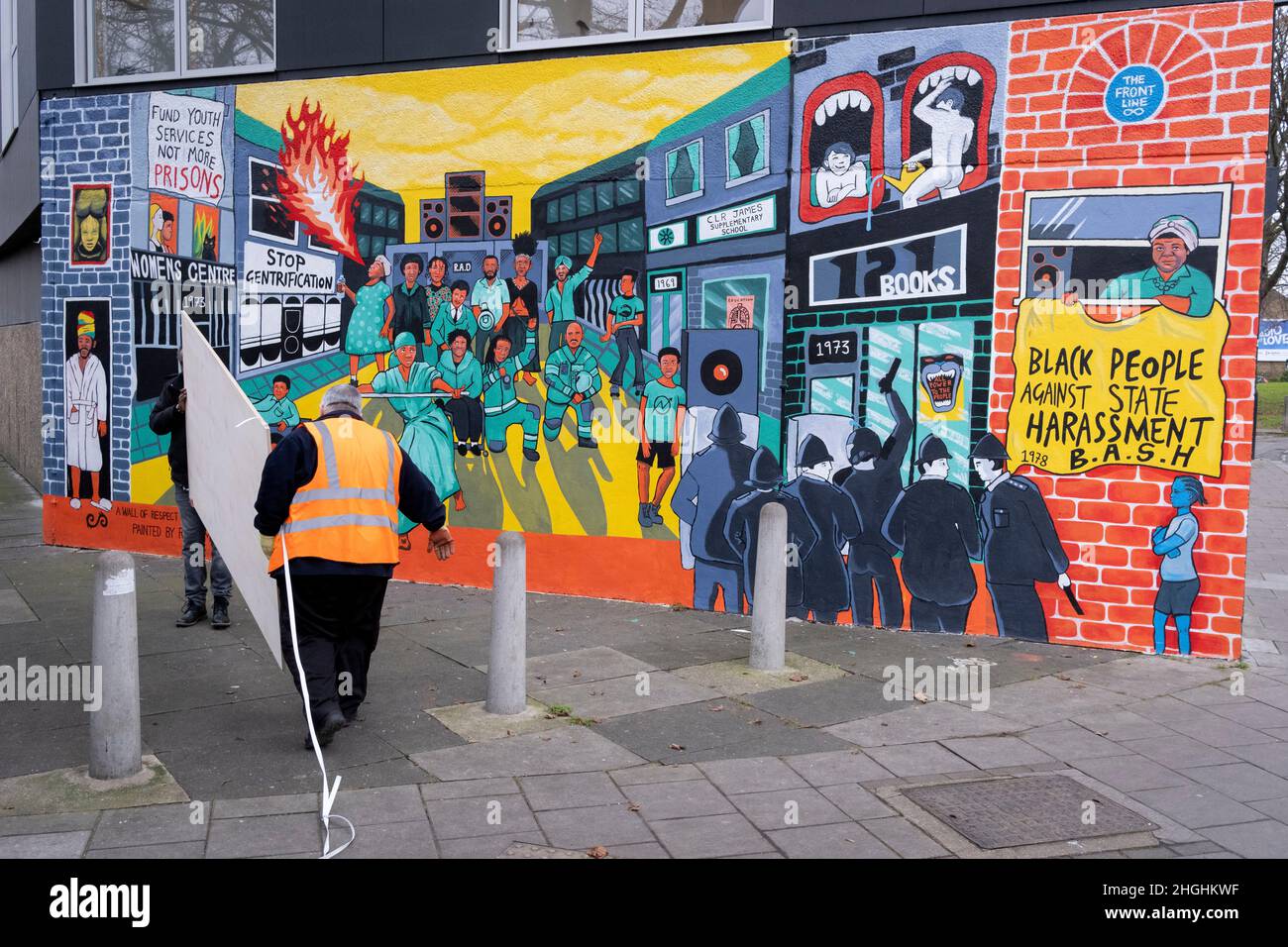 Two men carry supplies from a white van and past a mural that remembers