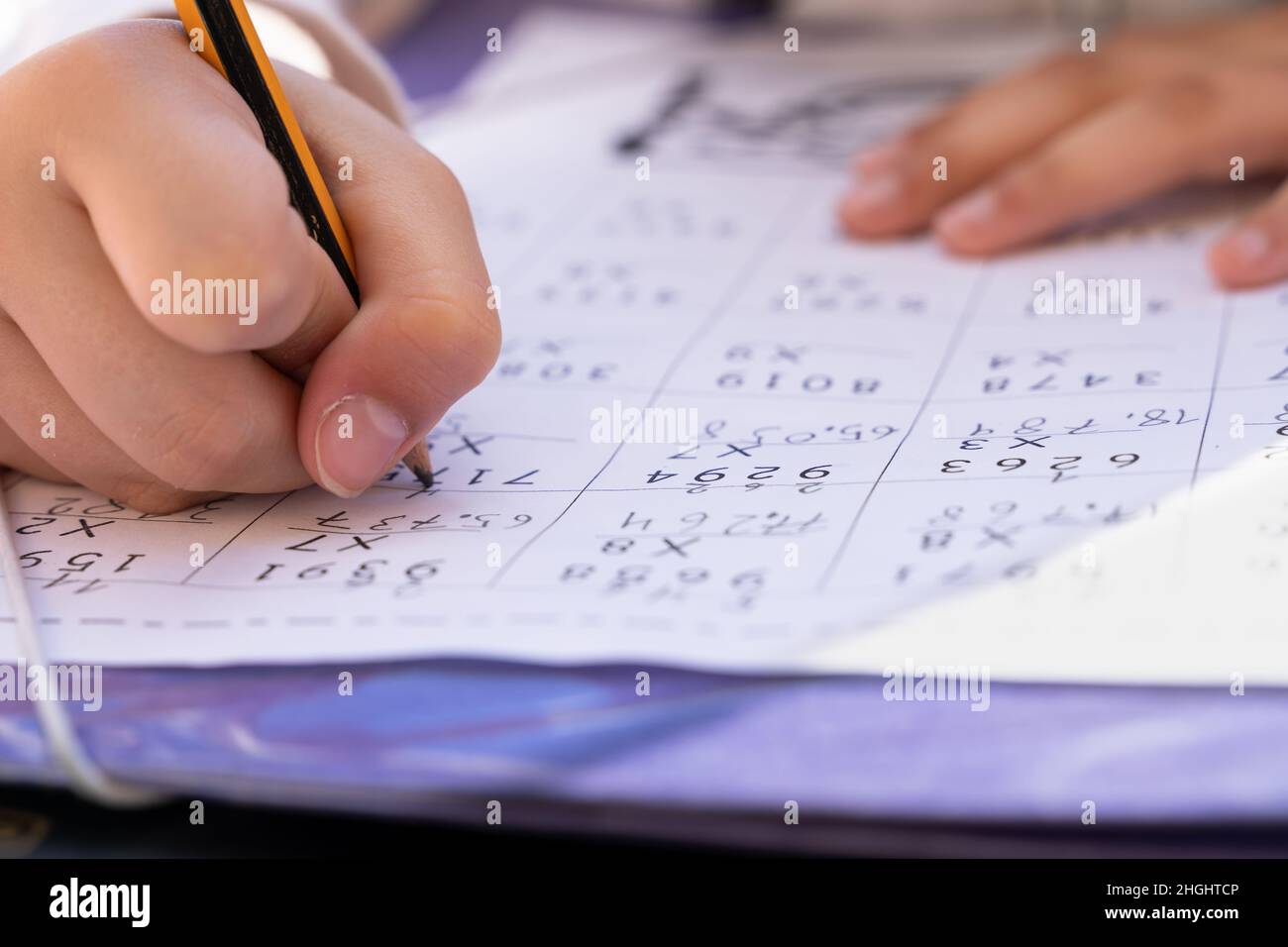 Close up on hands of little girl writing with pencil doing maths multiplication exercise sheet. School homework concept Stock Photo