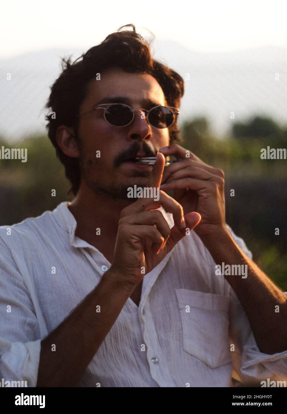 Young man in sunglasses playing mouth harp at sunset Stock Photo