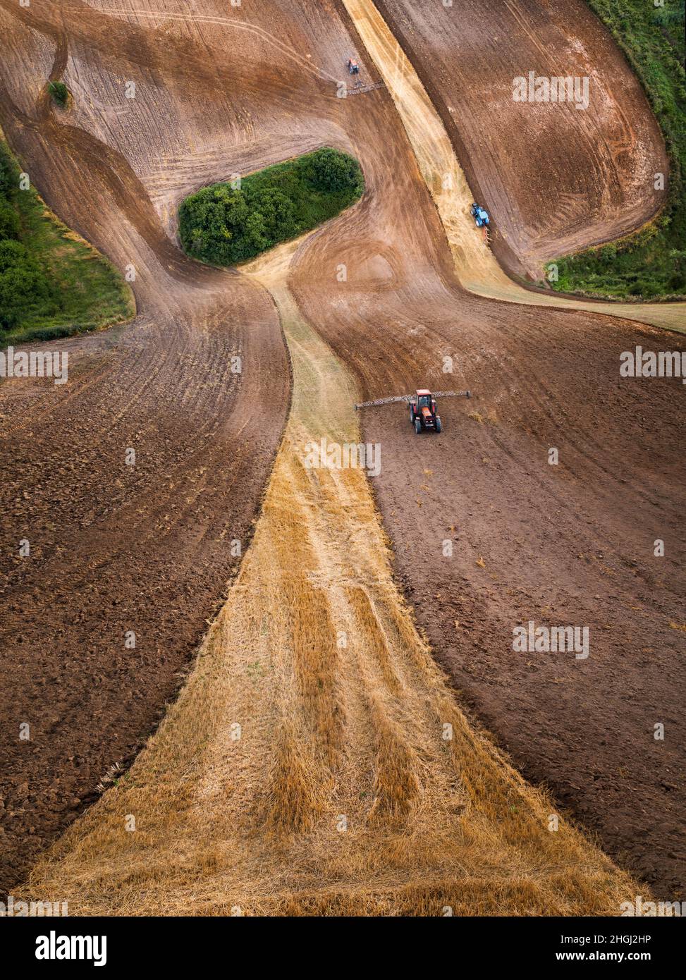 Tractors plowing the field on Mazury from the drone in wrapped perspective, Poland Stock Photo