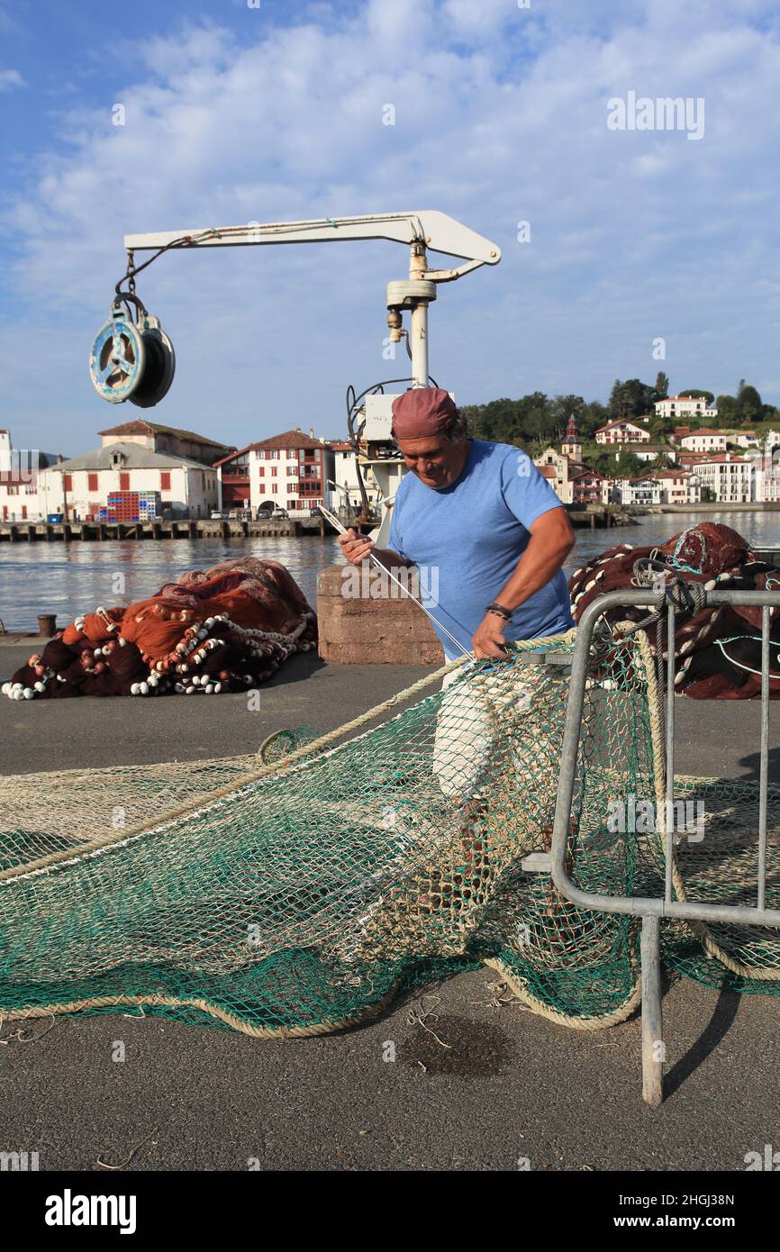 Local fisherman repairing his fishing nets on the quayside of St Jean de Luz harbour, Pays Basque, Nouvelle Aquitaine Stock Photo