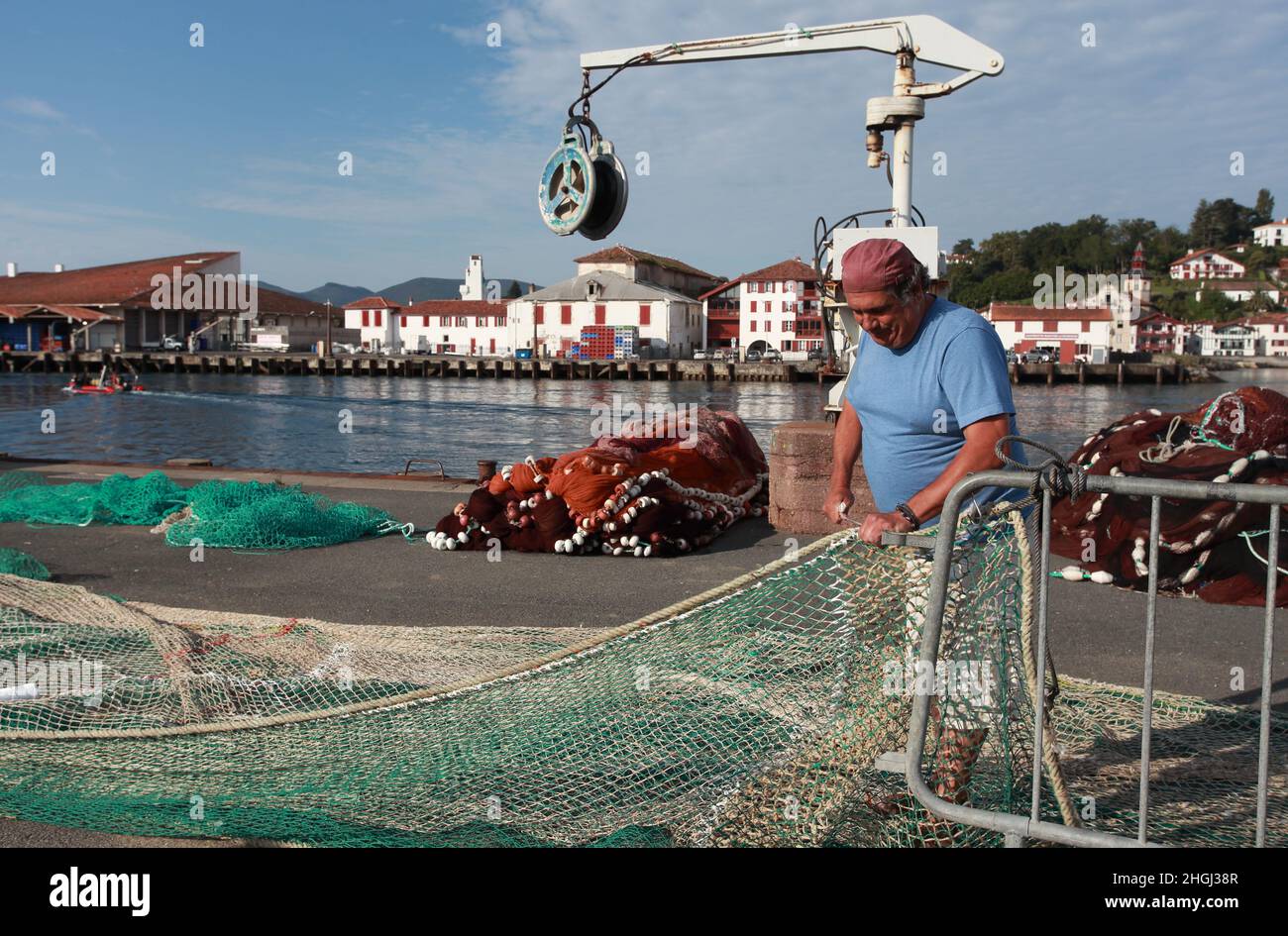 Local fisherman repairing his fishing nets on the quayside of St Jean de Luz harbour, Pays Basque, Nouvelle Aquitaine Stock Photo
