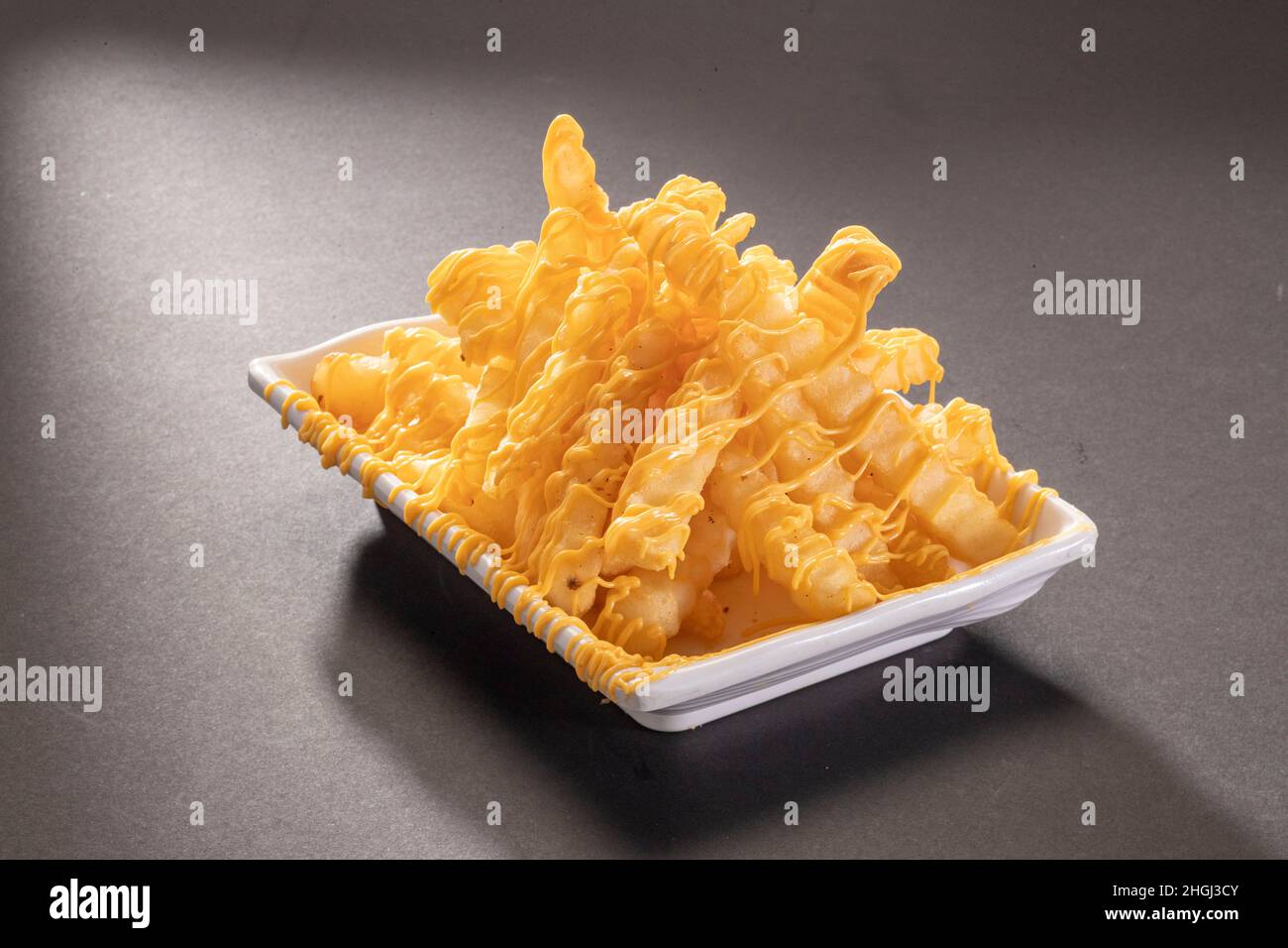 Cheese Fries Drizzle loaded or potato chips with cheddar cheese in white tray top view on dark grey background Stock Photo