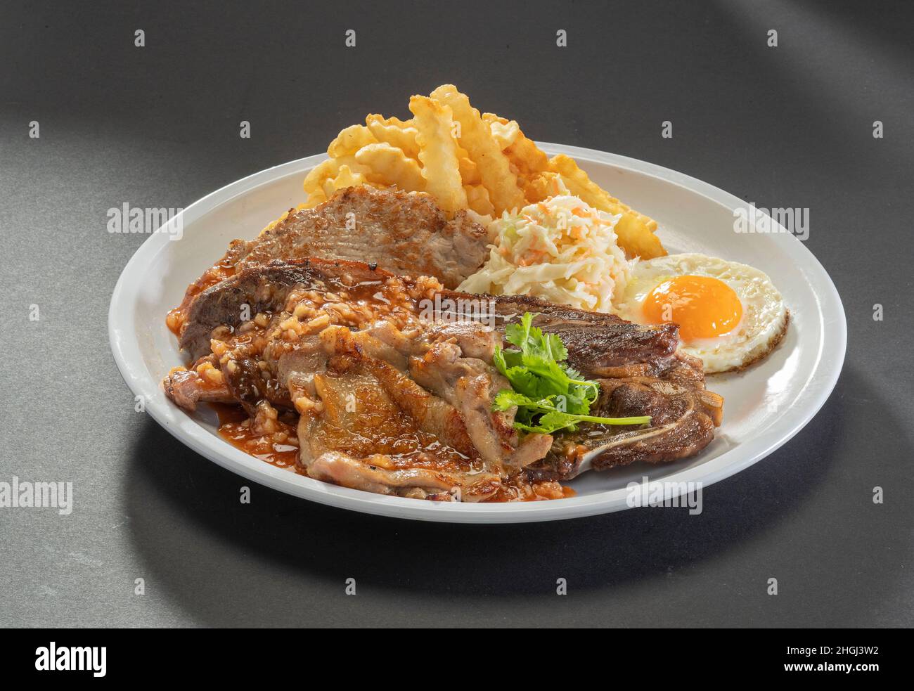Traditional mixed grill platter Grilled Lamb Chop, chicken cutlet, chicken chop, french fries, eggs and salad in white dish on dark grey background Stock Photo
