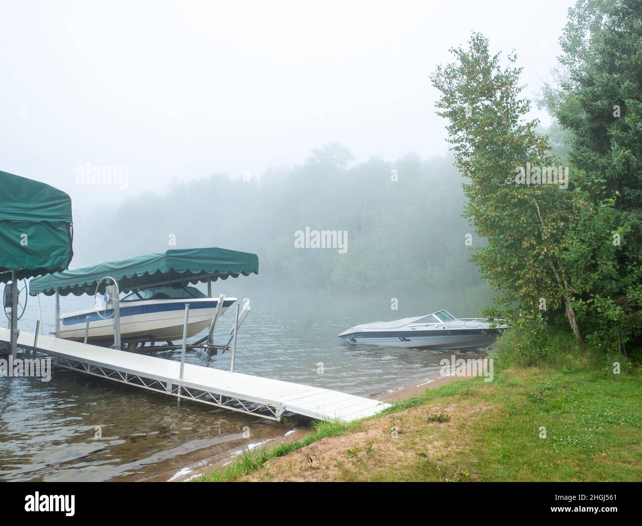 Beautiful Minnesota lake scene on a foggy morning with calm waters and a couple pleasure boats on shore. Stock Photo