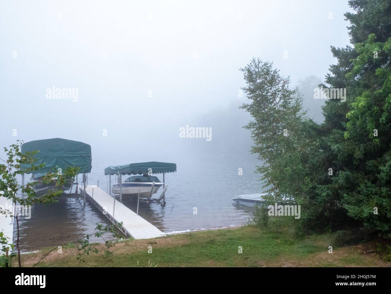 A foggy morning on a beautiful Minnesota lake, with calm waters, a dock, and pleasure boats on shore and on boatlifts. Stock Photo