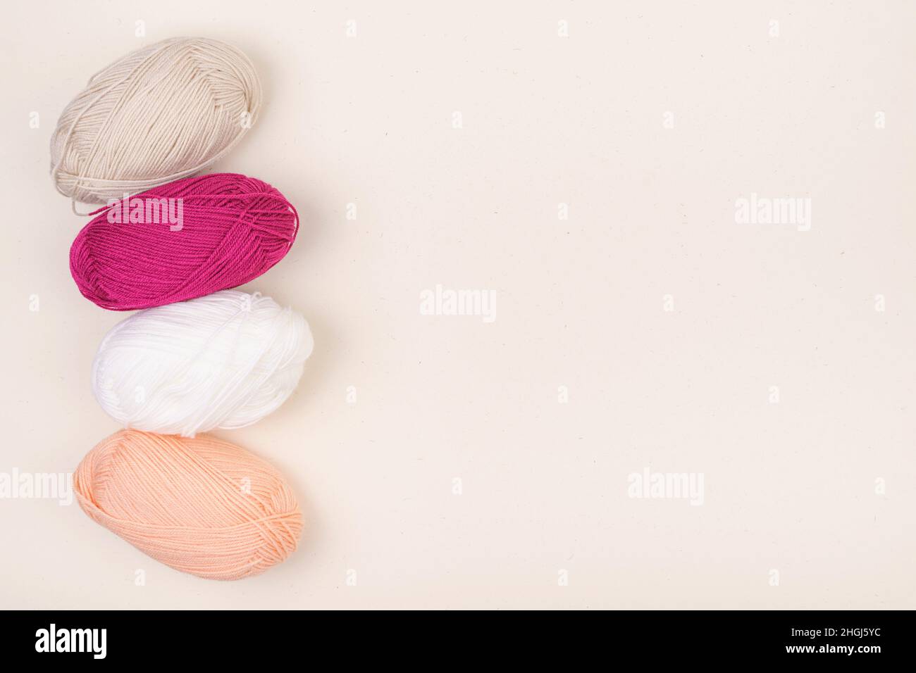 Colored balls of yarn is beige, light pink and white. Skeins of yarn with empty space for your text or advertising on a beige background. Stock Photo