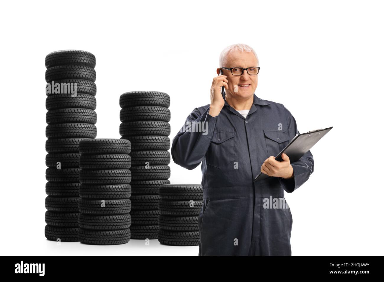 Auto mechanic making a phone call next to a pile of car tires isolated