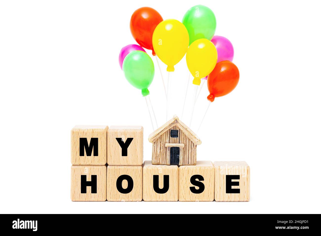 Text MY HOUSE made of wooden letter blocks and a miniature house model with toy balloons isolated on white background. Creative housewarming party con Stock Photo