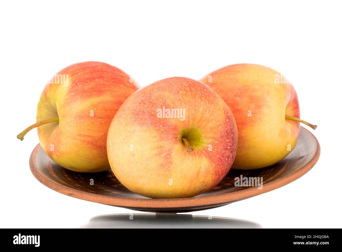Three red juicy apples on a clay plate, macro, isolated on white. Stock Photo