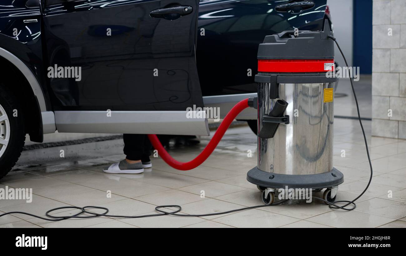 A worker vacuums the interior of a car at a car wash. Vacuum cleaner
