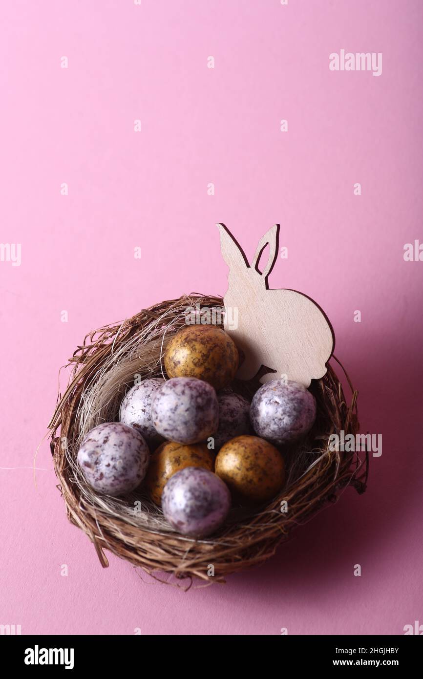 Easter concept - rabbit in a nest with chocolate eggs against pink ...