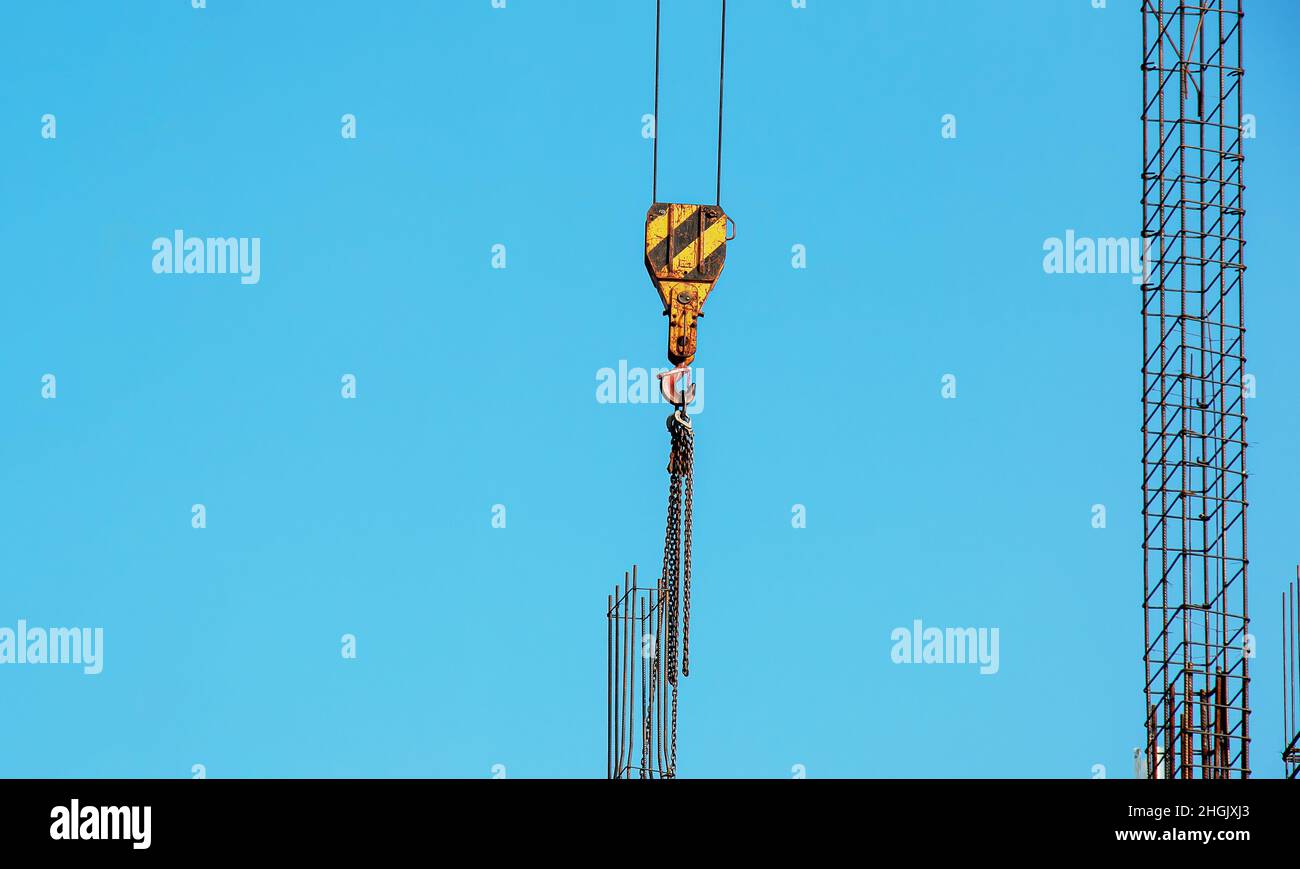 Hooks hanging from large crane chains descending from above. Blue sky background. Stock Photo