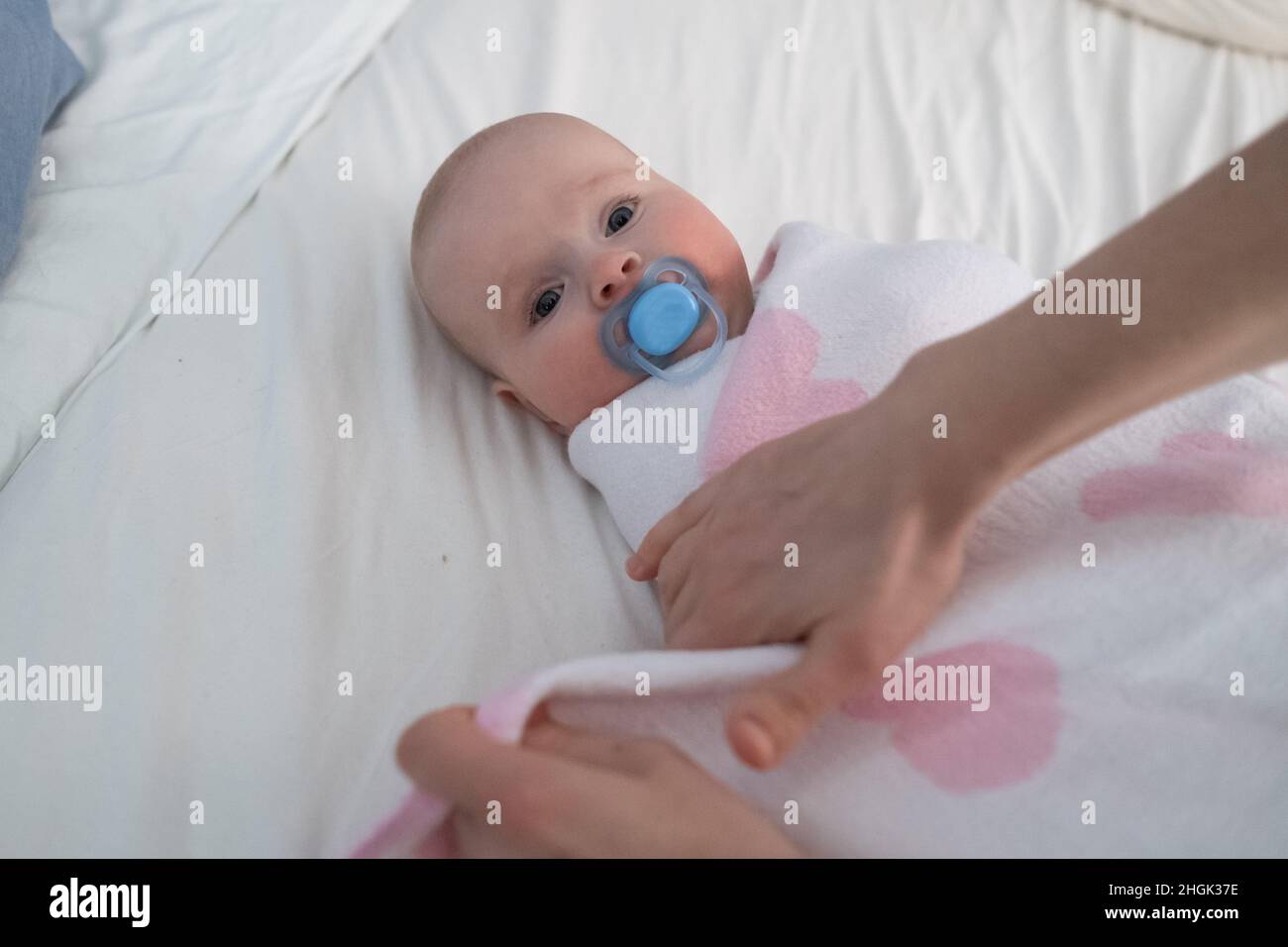 Mother preparing her newborn baby for rest swaddling in a blanket Stock