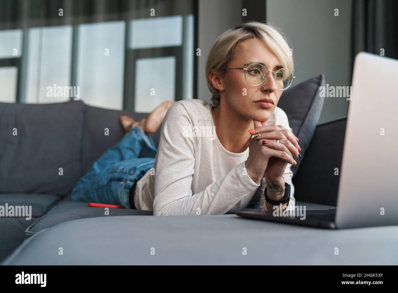 Upset frustrated mid aged blonde woman looking at laptop comouter screen on a couch at home Stock Photo