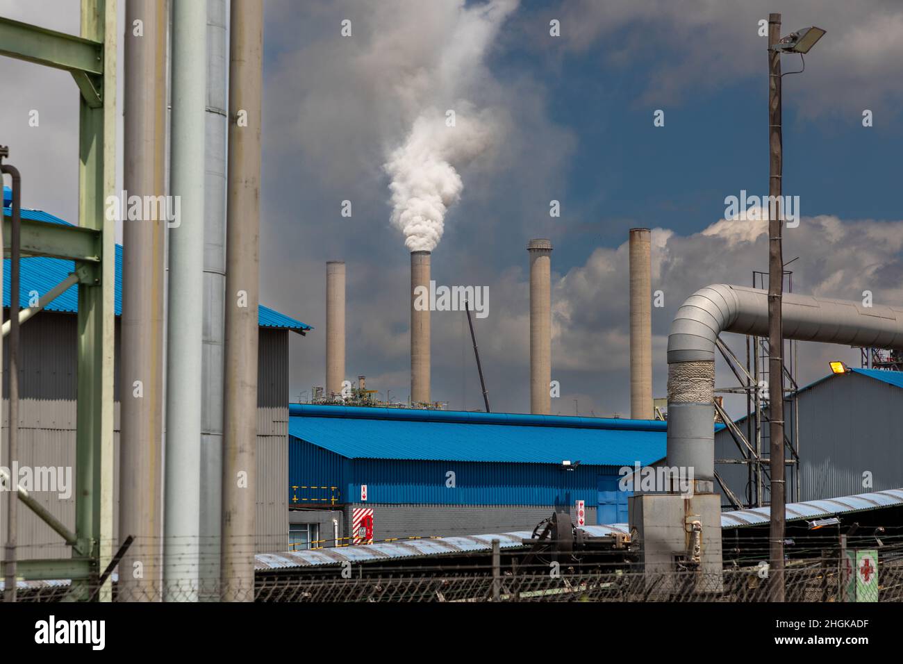 Industrial site with thick white smoke rising from one of the concrete smoke stack. Concept for global warming due to burning of fossil fuel. Stock Photo