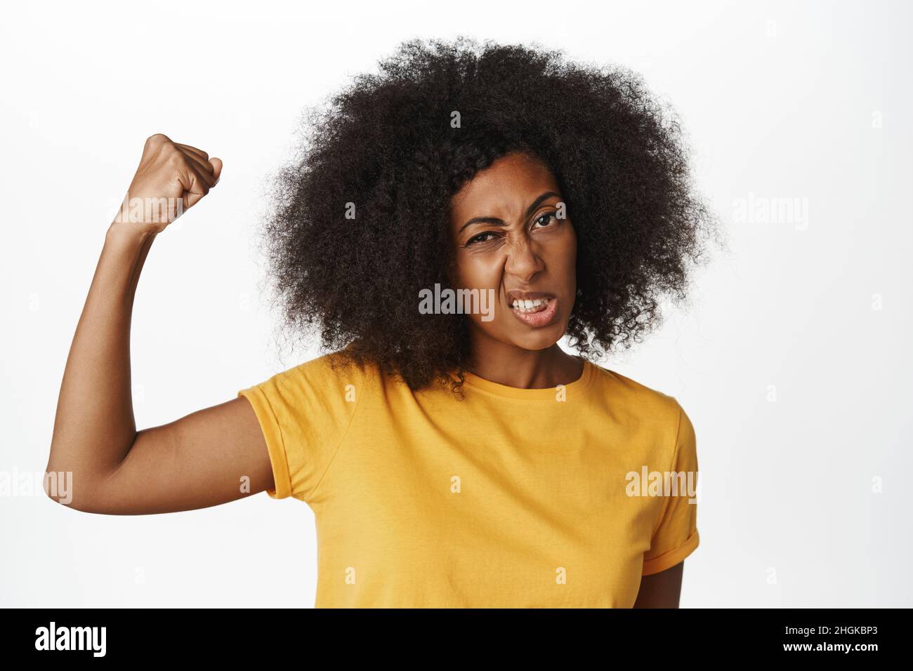 Women power. Strong and powerful african american woman flexing biceps and shows teeth fearless, brags her strengths, standing over white background Stock Photo