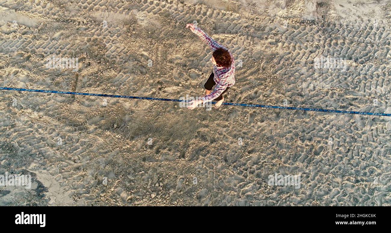 Aerial view above male slackliner balancing on rope and doing acrobatics, demonstrating agility, Pacific Beach in San Diego, California, USA Stock Photo