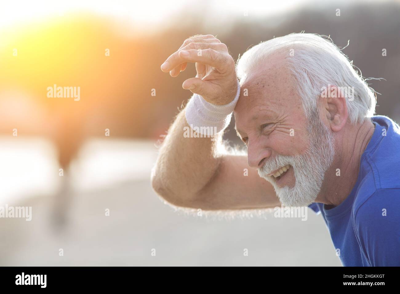 Tired senior bearded man wiping sweat from his forehead with wristband after outdoor exercise Stock Photo