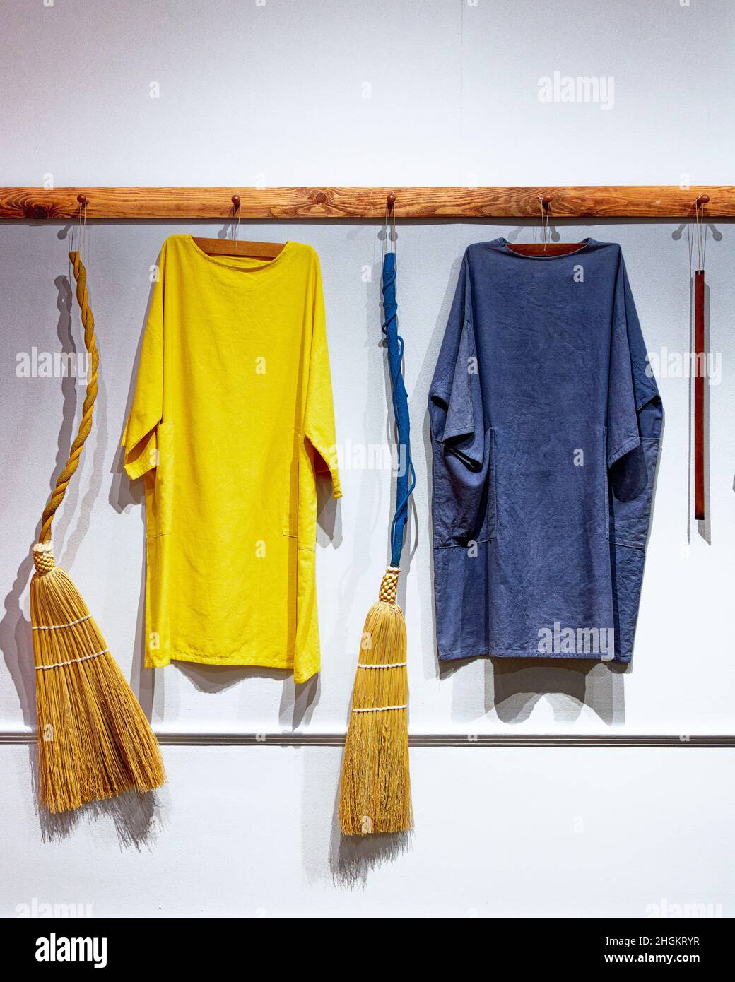 Colorful tunics and straw brooms hang on wall at Fruitlads Museum. Harvard, Massachusetts Stock Photo