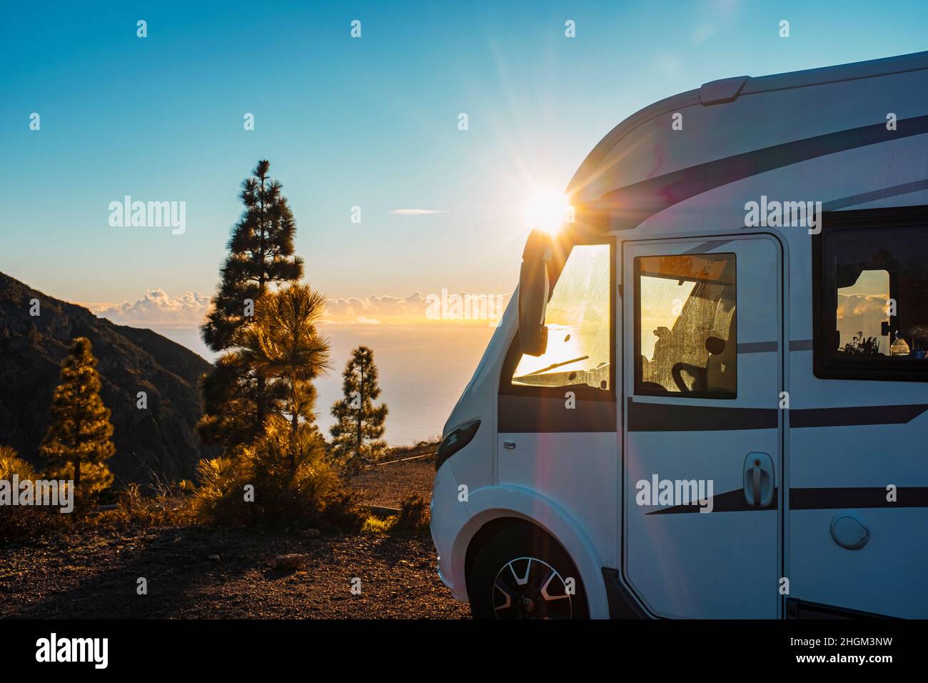 Beautiful sunset in background and modern camper van parked in the nature to enjoy freedom and vanlife alternative lifestyle. Travel people family and Stock Photo