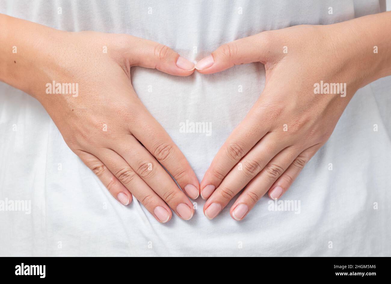 Heart shaped hands of a young woman touching her belly Stock Photo