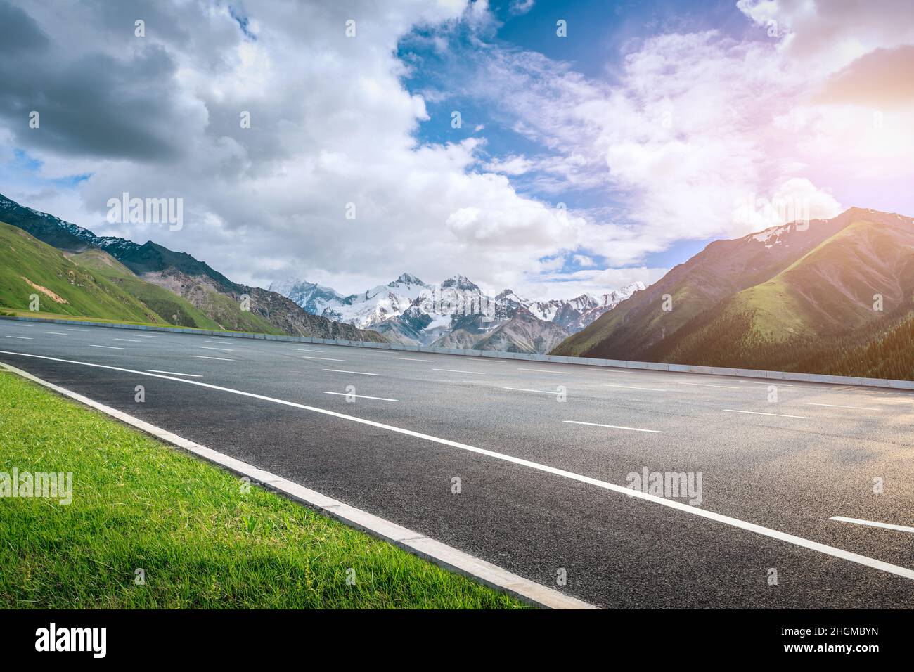 Asphalt road and snow mountain under blue sky. Highway and mountain background. Stock Photo