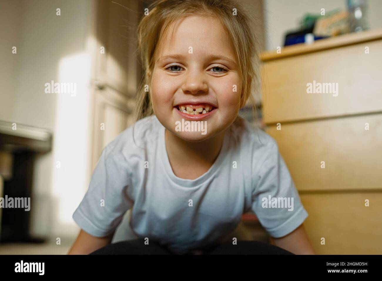 Child girl with blue eyes is having fun at home on floor, looking straight in camera. Stock Photo
