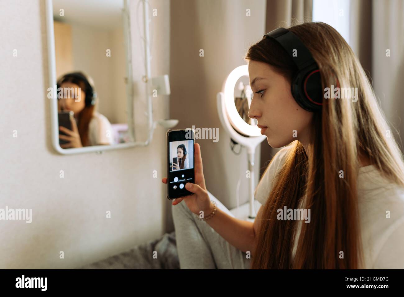 Teenage girl in headphones in front of the mirror takes selfie, admires. Stock Photo