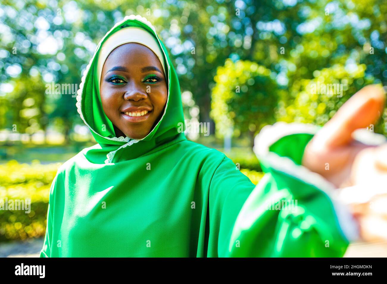 latin hispanic arab woman in green muslim dress with modern bright make up and nose piercing taking selfie at phone camera outdoors Stock Photo