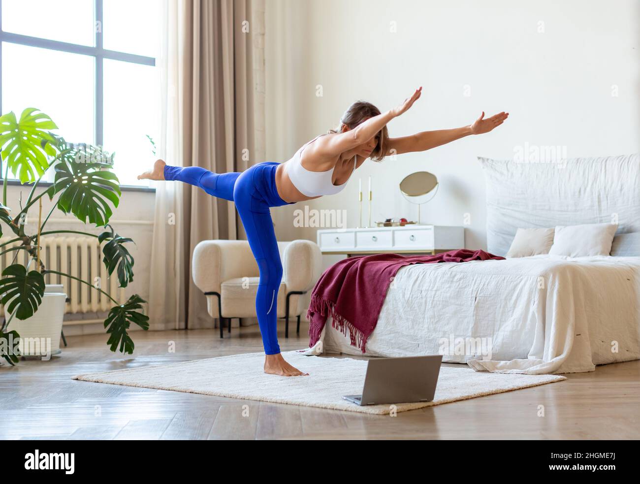 A middle-aged woman is engaged in pilates at home in front of a laptop monitor. Healthy and active lifestyle concept. Stock Photo