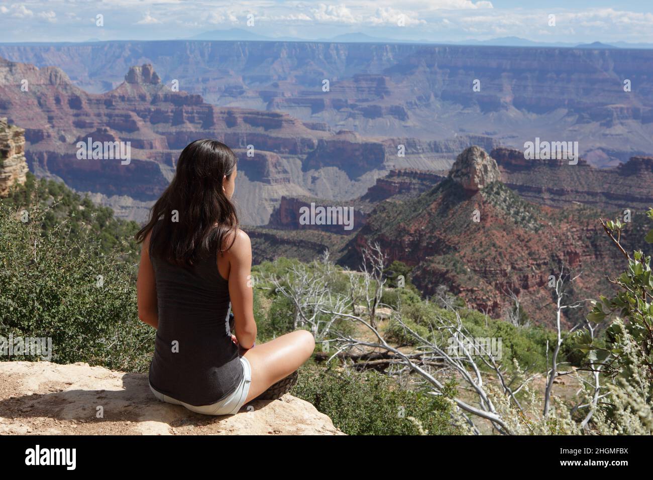 A sitting young female hiker takes in the view from the North Rim of the Grand Canyon at Widforss Point Stock Photo