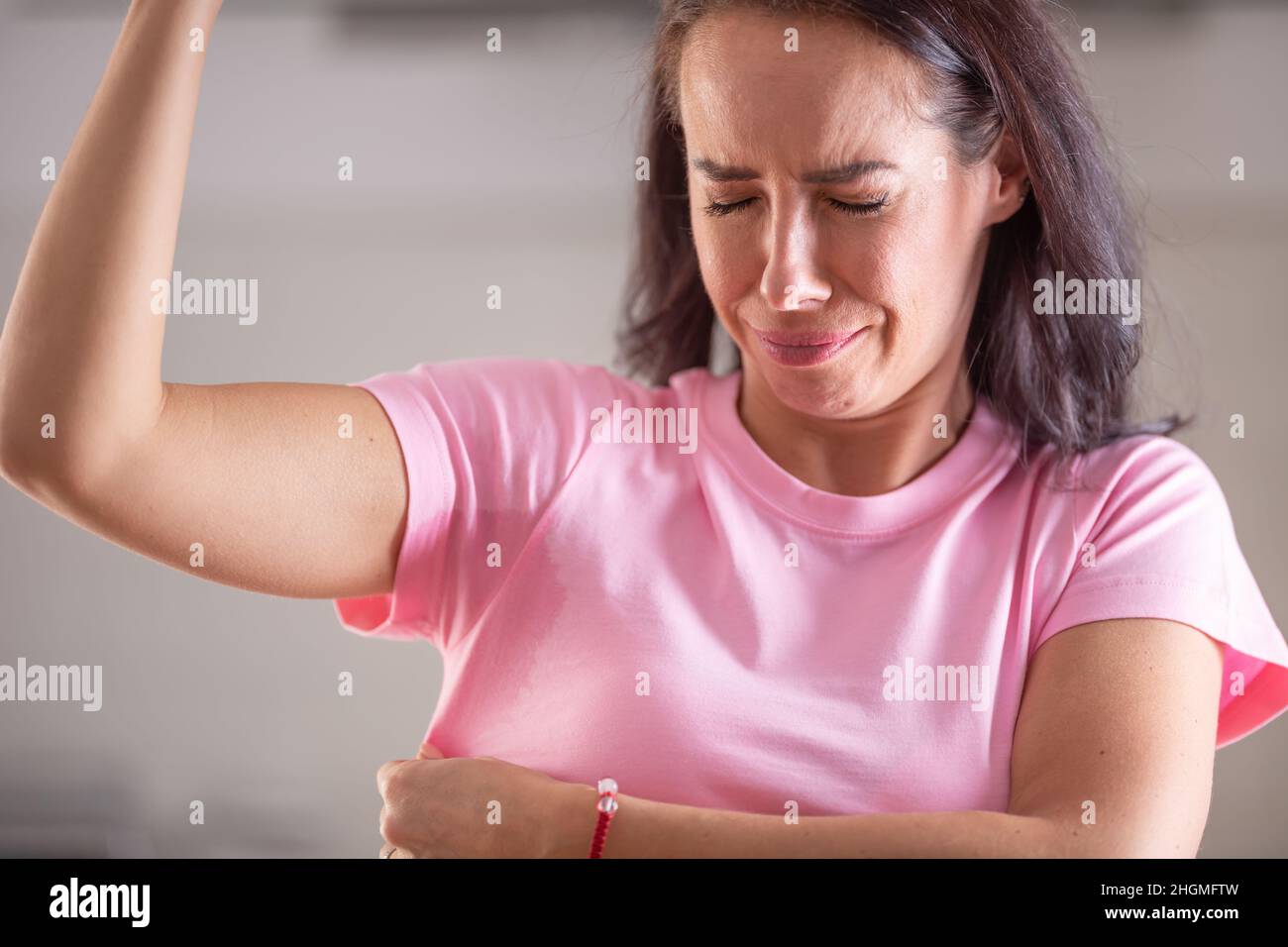 Woman Smells Herself With Repulsive Facial Expression And Sweat Patches On Her Pink Shirt Stock