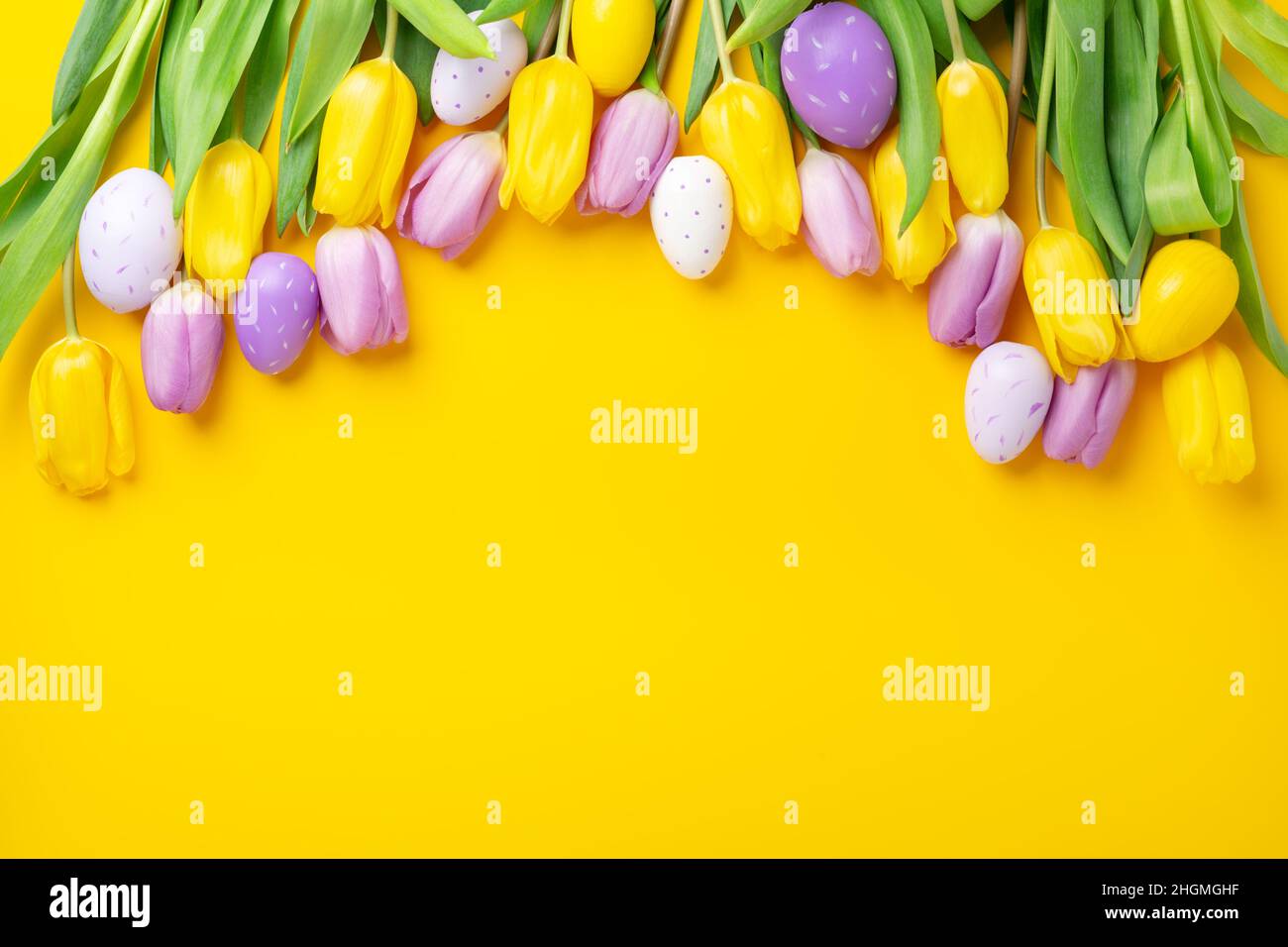 Easter greeting card. Multicolored easter eggs and tulips on yellow background. Easter concept Stock Photo