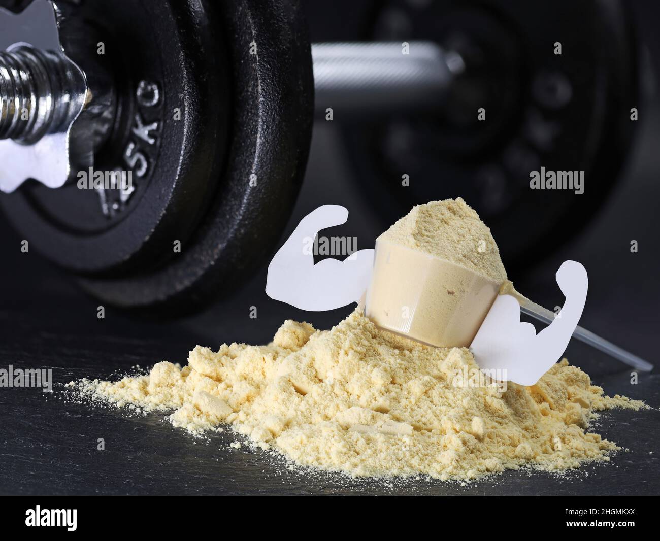 Whey protein scoop with mucles on powder heap with dumbbell on black background, muscle gain from protein shakes Stock Photo